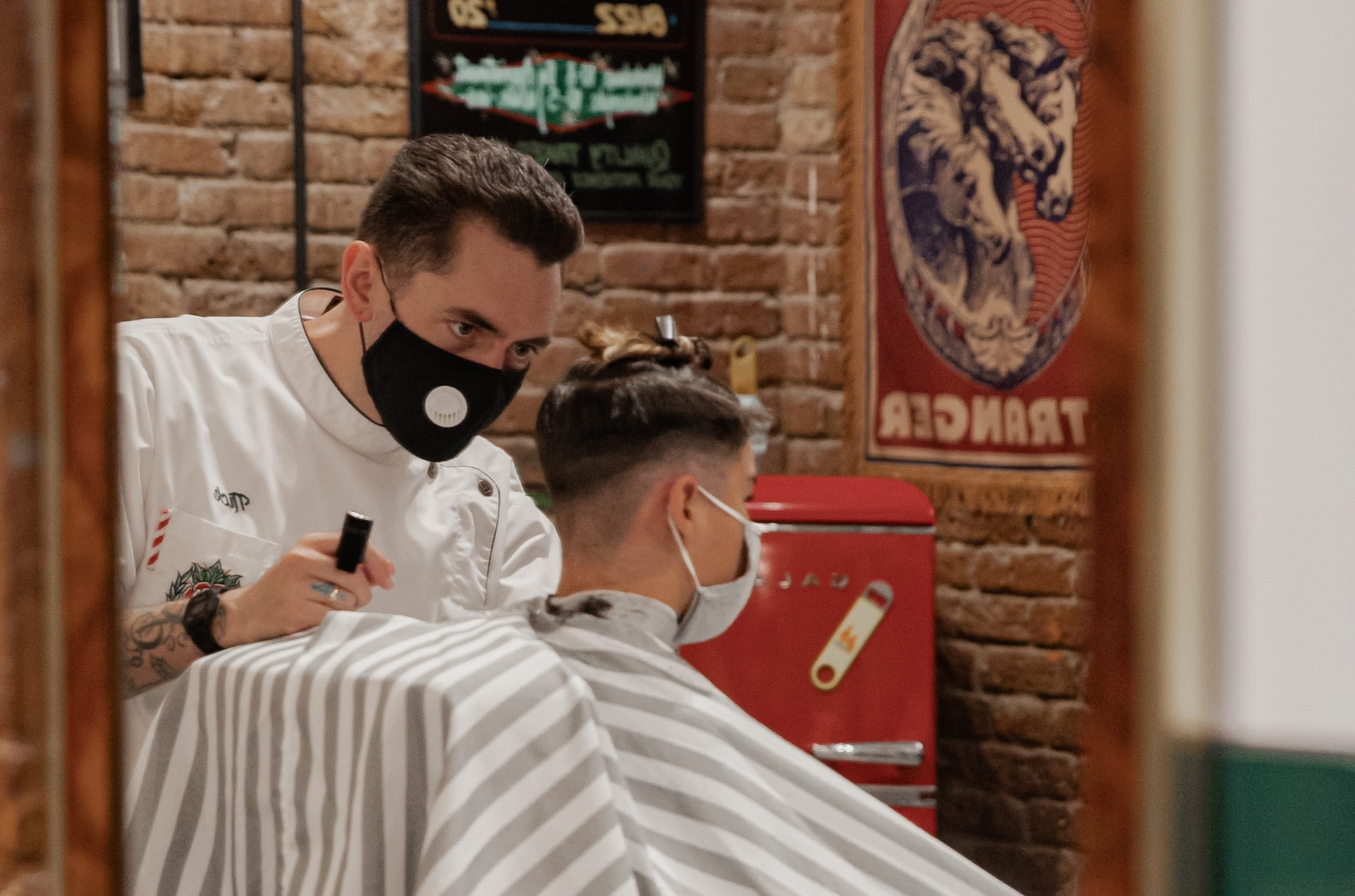 Hairdresser is cutting the hair of his client – both wear a face mask